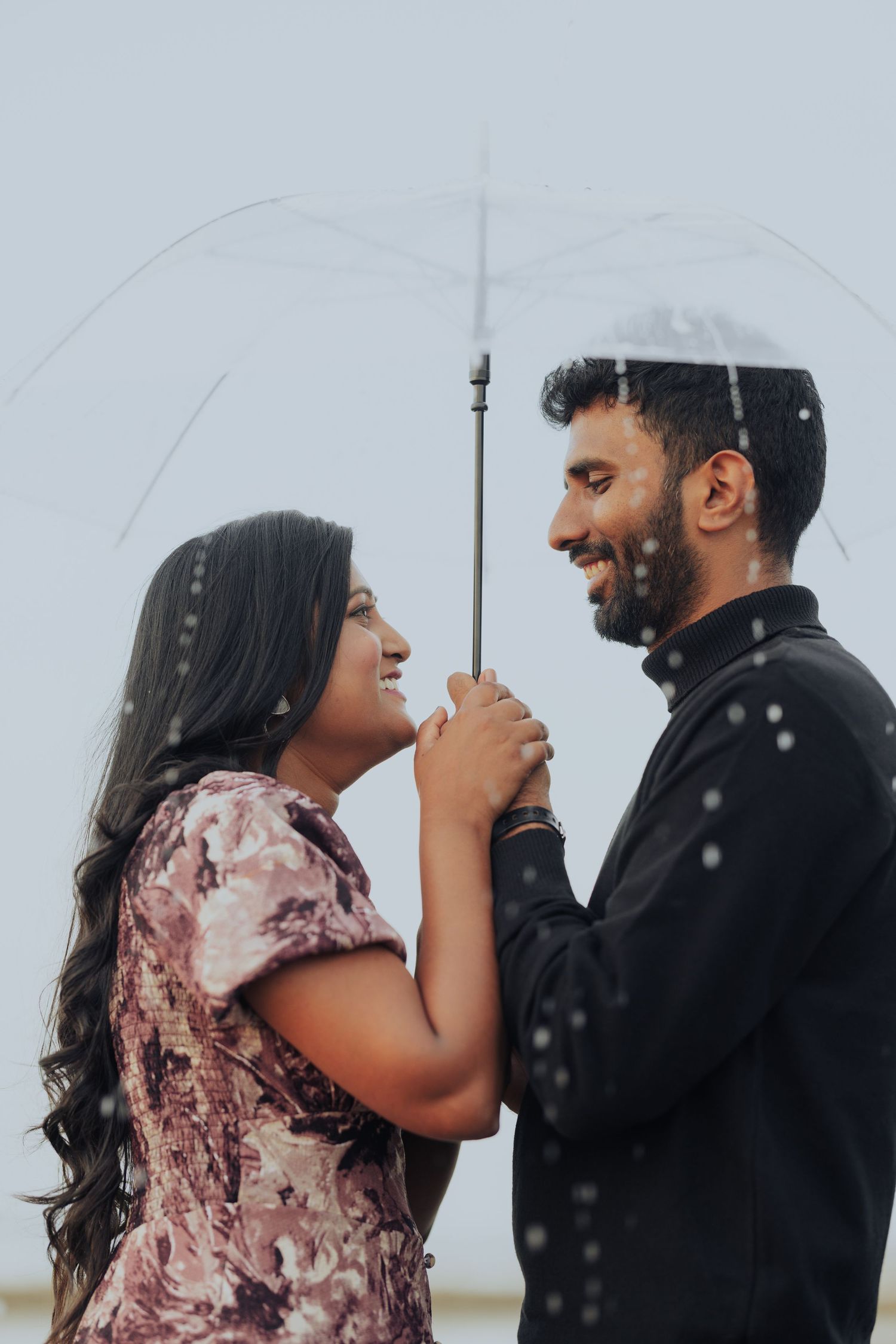 Indian bride and groom in traditional attire laughing and touching foreheads in a joyful close-up.