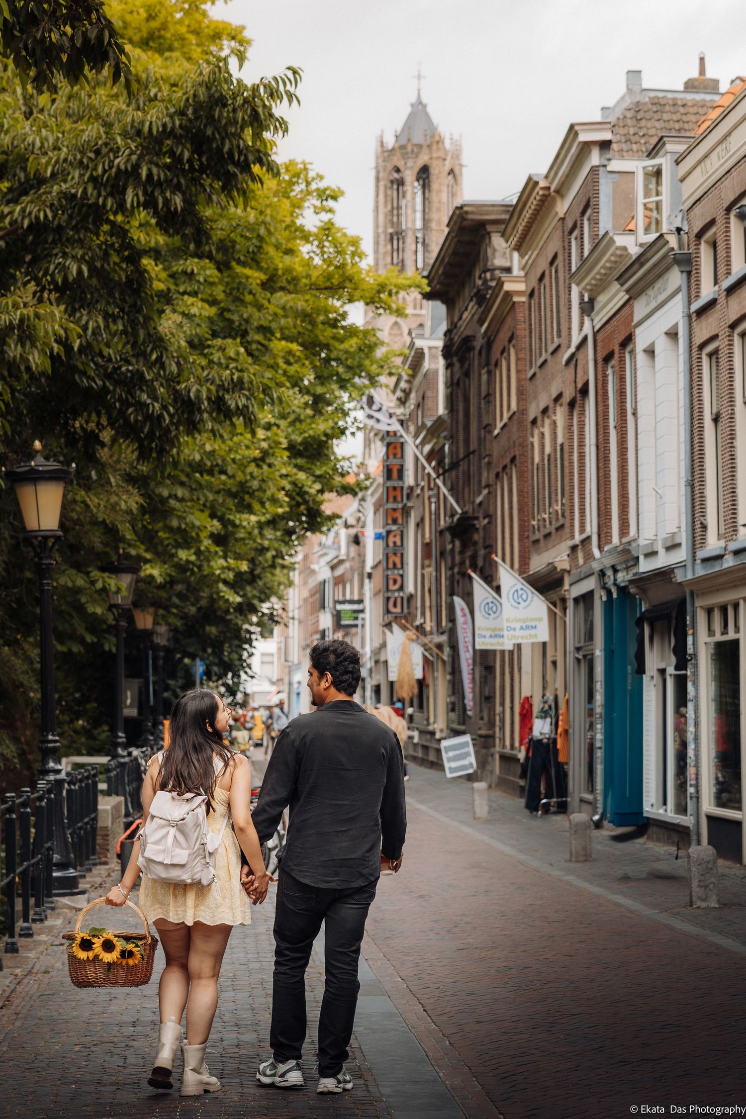 Couple holding hands walking down a charming Utrecht street with the iconic Dom Tower visible in the background.