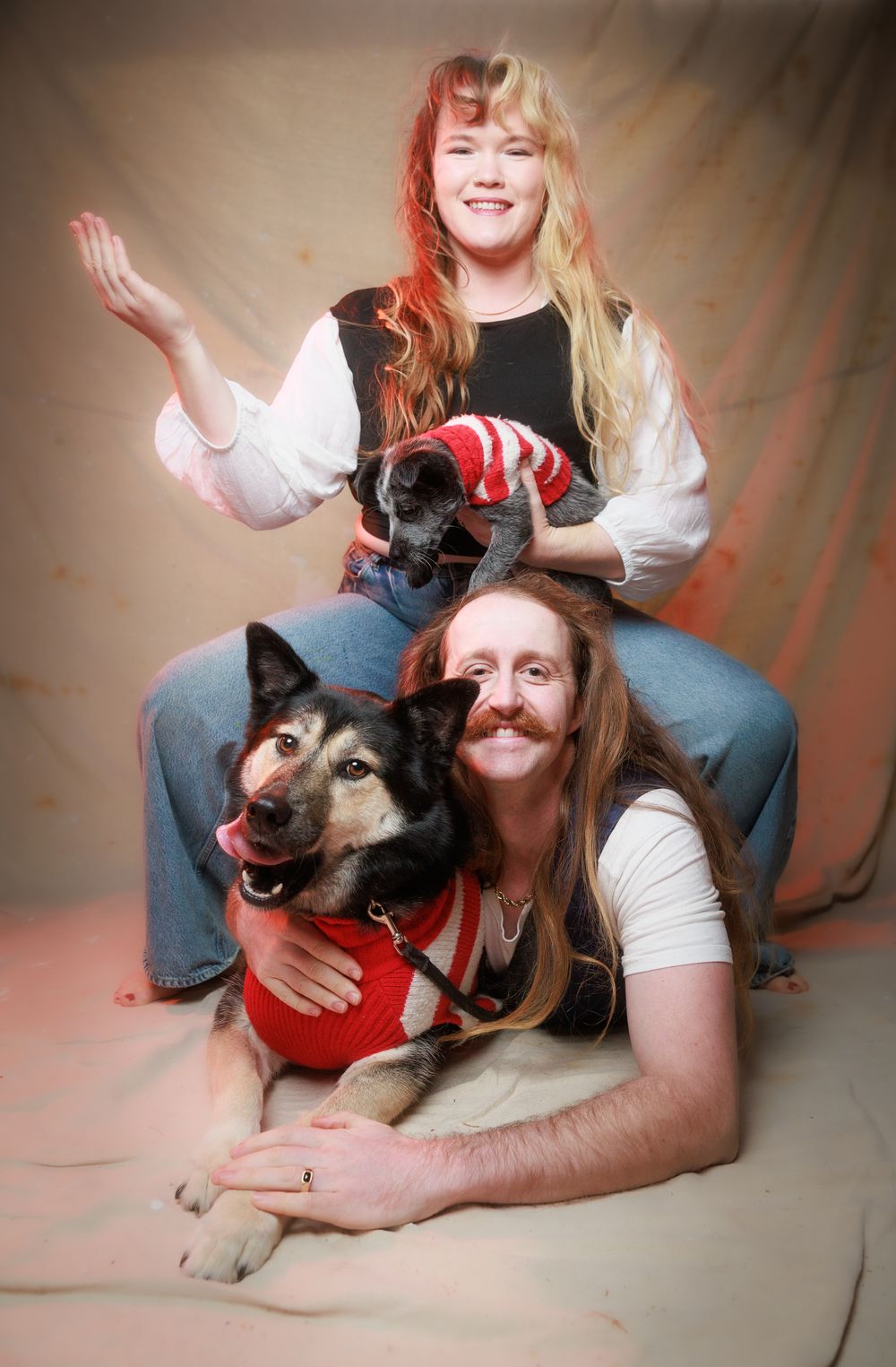 Two people pose with a German Shepherd dog and small pet in a vintage studio portrait photo.