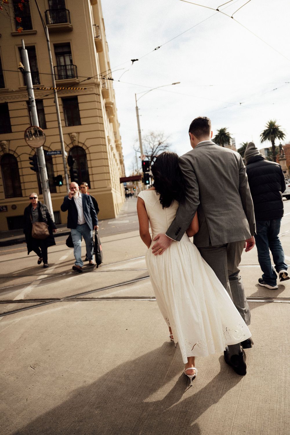 Bride and groom walking arm in arm across a city street intersection on their wedding day.