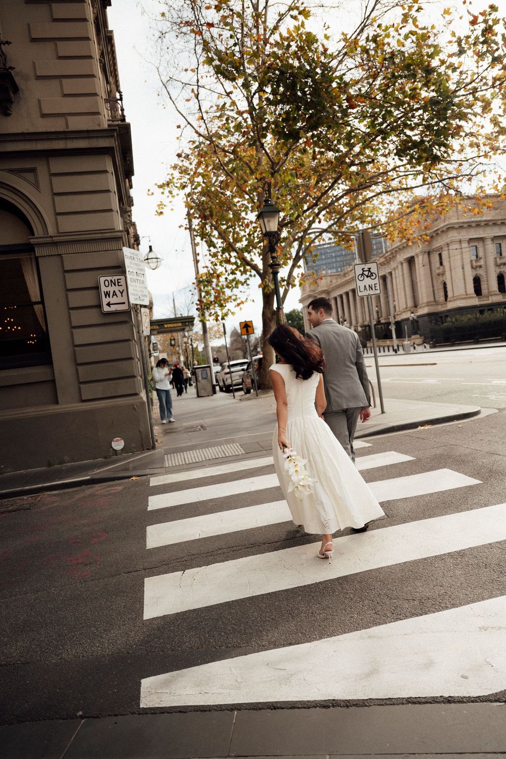 Bride and groom crossing a zebra crossing in a city street, bride wearing a white wedding dress.