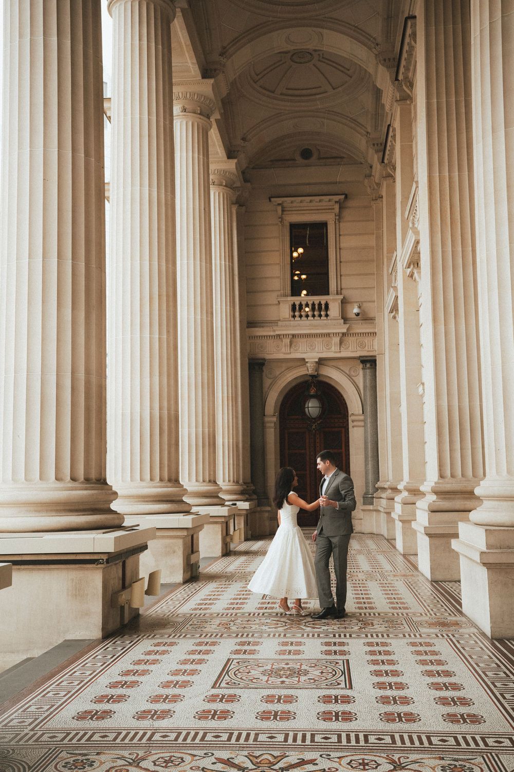 Bride and groom share a romantic moment among grand classical columns on their wedding day.