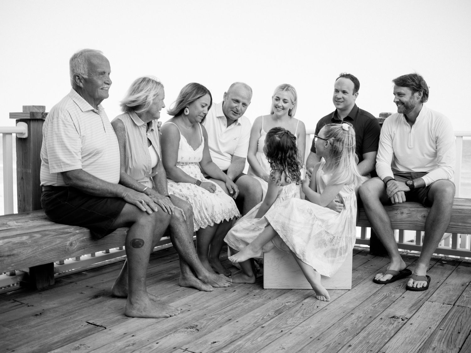 Black and white family portrait on a wooden deck, multi-generational group smiling and laughing together outdoors.