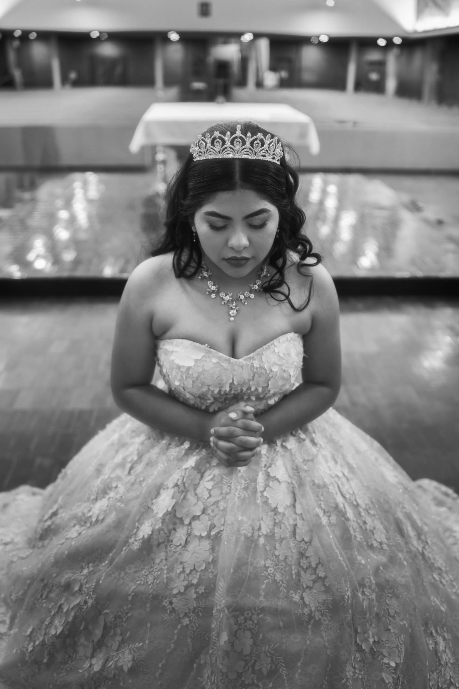 Young woman in blue dress and crown poses with gold number 15 balloons in green field for quinceañera photos.
