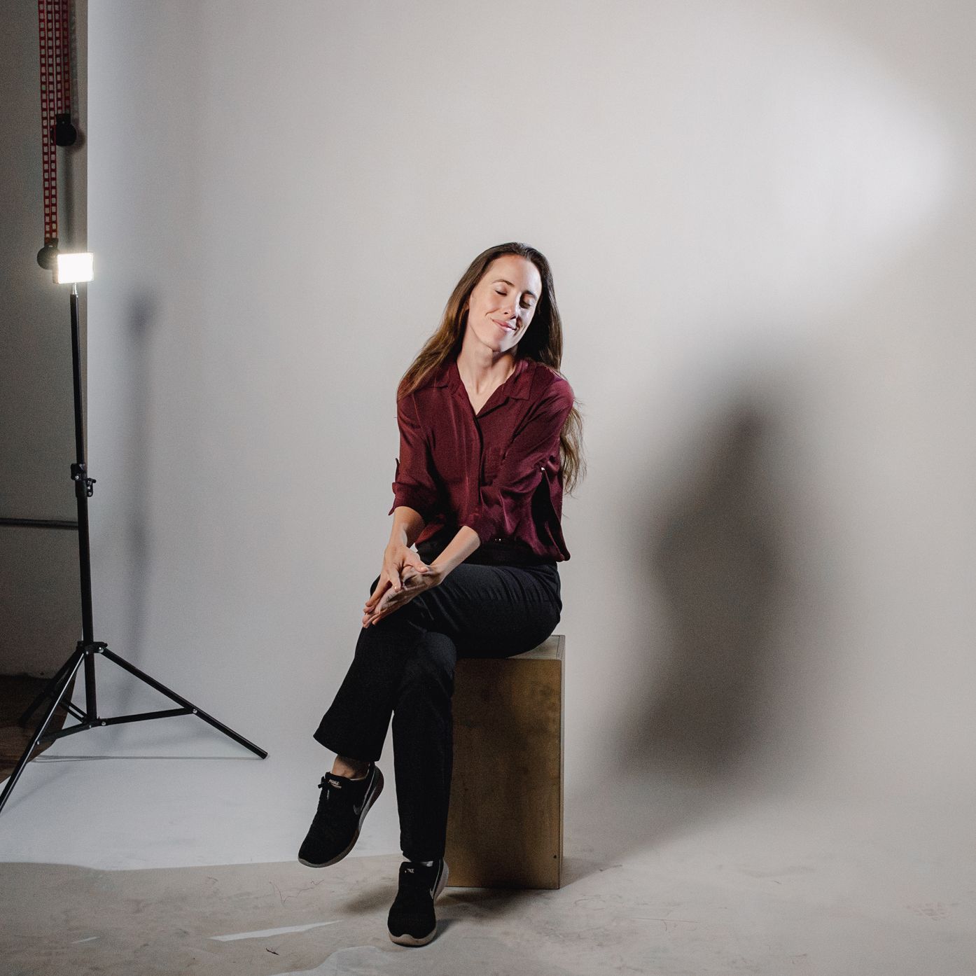 Woman posing with shopping bag in professional photo studio with white backdrop and studio lighting equipment.