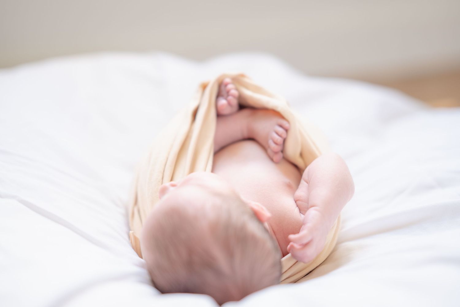 Close-up of a newborn baby's tiny feet and toes resting on a soft white fluffy blanket in a light blue onesie.