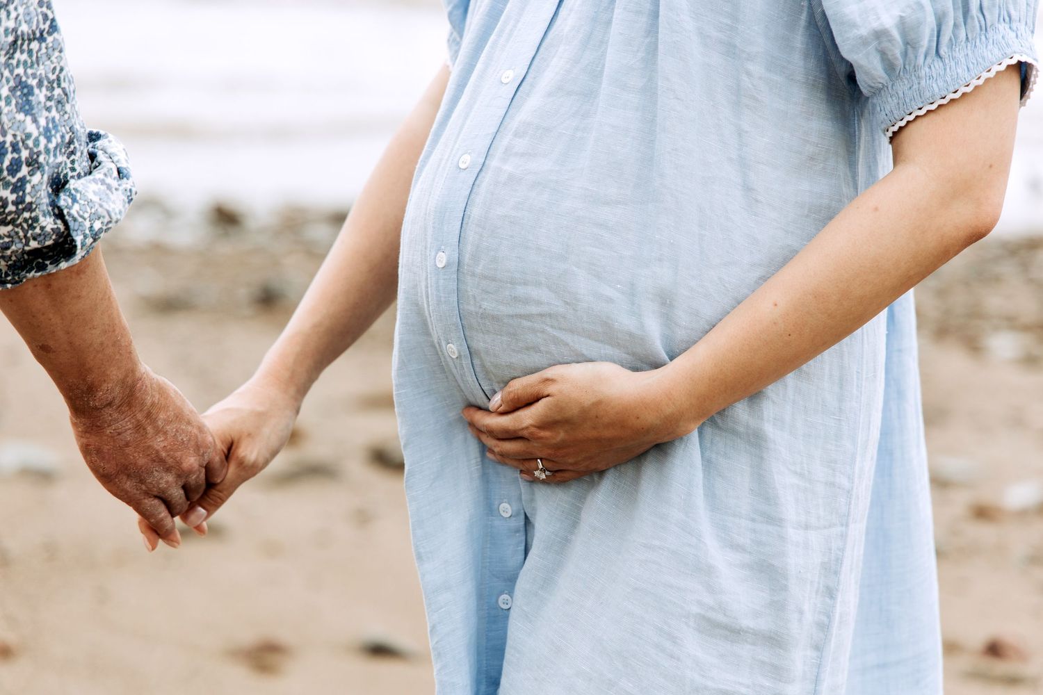 Expectant couple holding hands beside the sea during a relaxed maternity photography session.