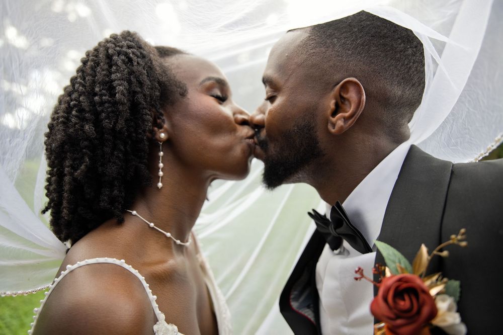 A bride and groom share a romantic kiss under a flowing white veil on their wedding day.