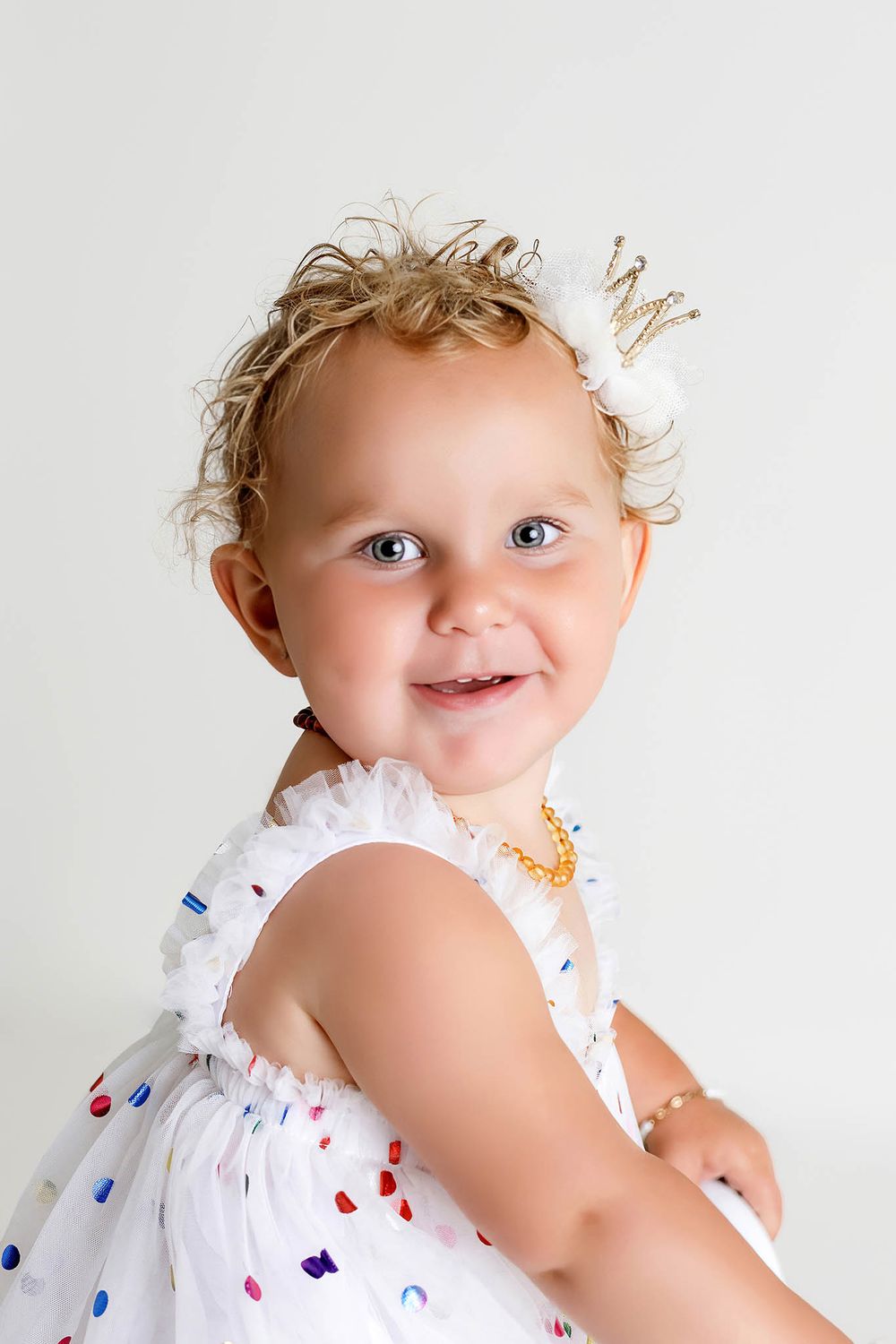 Smiling two year old girl in confetti dress, by affordable 2nd birthday photographer.