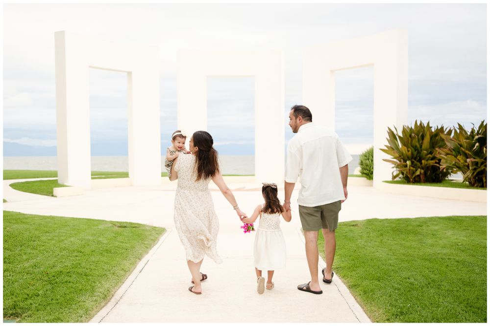 Riviera Nayarit family photographer, family of four walking hand in hand toward white arches overlooking the ocean at Grand Velas.
