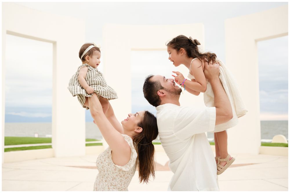 Puerto Vallarta family photography, joyful family lifting two young daughters in the air at a white columned seaside venue.