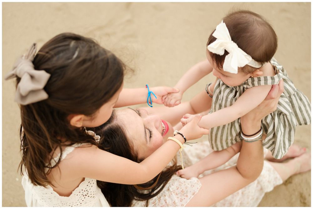 Riviera Nayarit family photographer, mother and two young daughters sharing a joyful moment on the beach with matching hair bows.