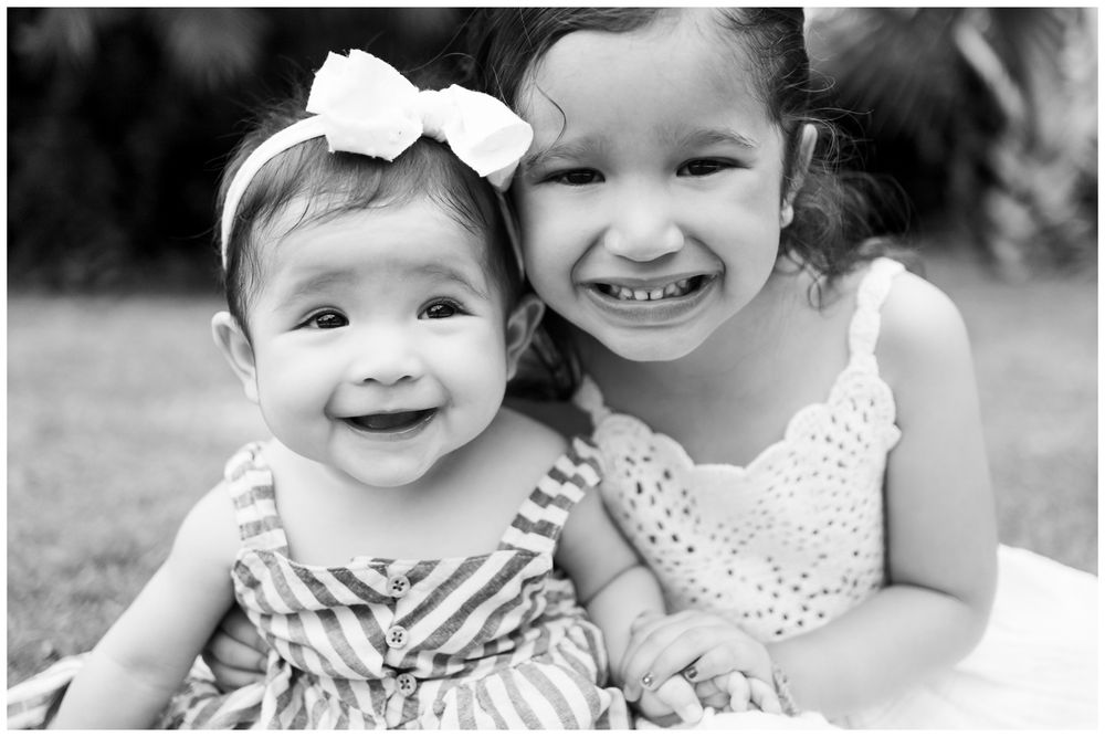Sayulita family photography, two young sisters smiling together outdoors with tropical greenery in the background.