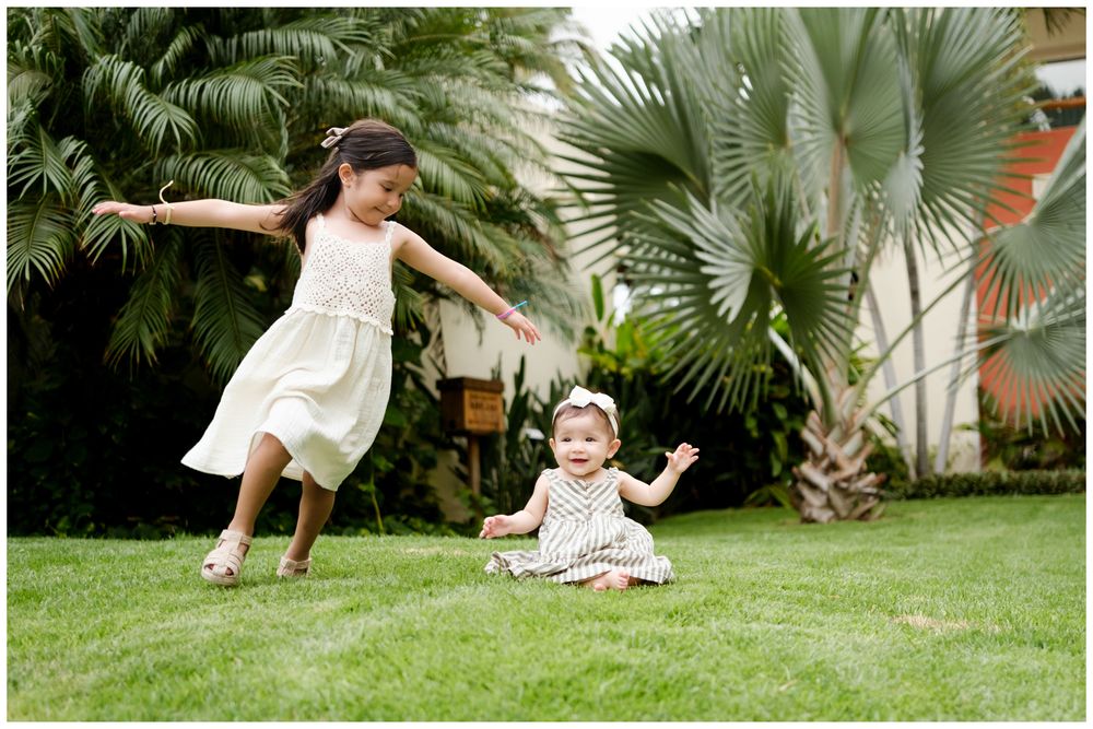 Riviera Nayarit family photographer, two young sisters playing on green lawn with tropical palm trees in the background.