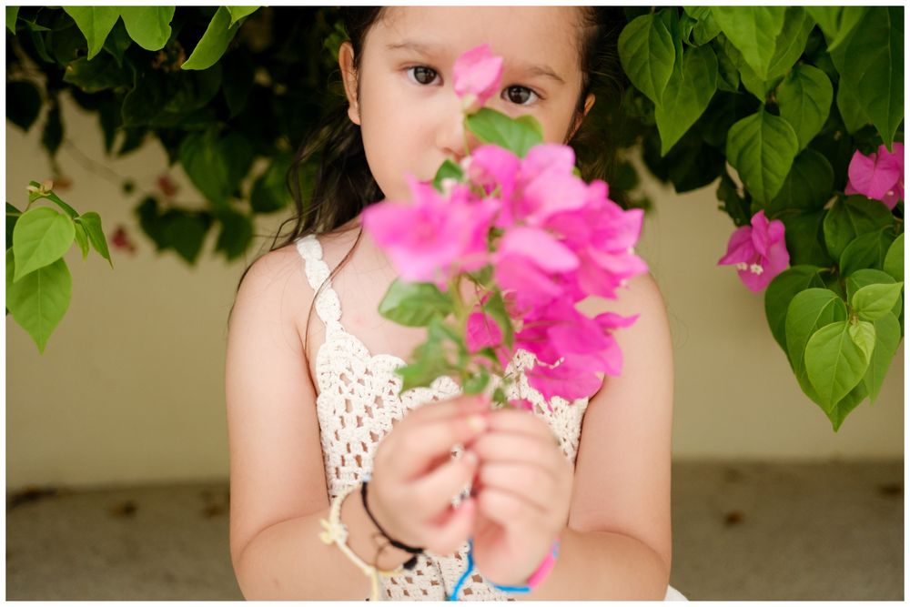 Riviera Nayarit family photographer, young girl holding vibrant pink bougainvillea flowers near lush green tropical plants outdoors.
