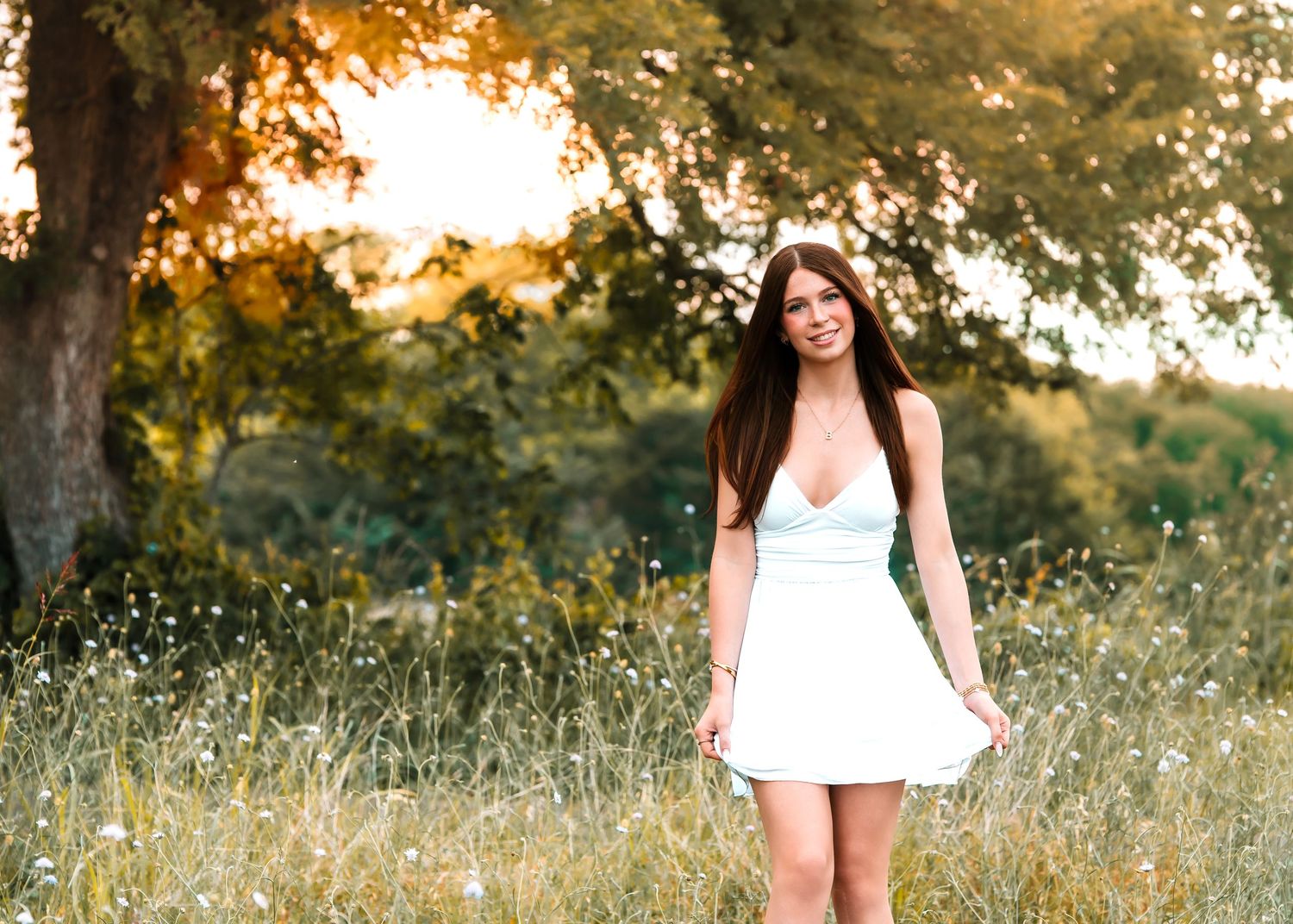 Young woman in floral dress smiling among hay bales in golden field at sunset.