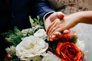 Couple holding hands with diamond engagement ring resting on a bridal bouquet of white and red roses near Knoxville, TN.