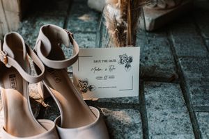 Elegant white bridal heels beside a floral save the date card on rustic stone tiles near Knoxville, TN.