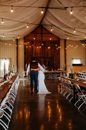 Bride and groom share first dance in rustic barn wedding venue with string lights and draped fabric ceiling near Knoxville, TN.