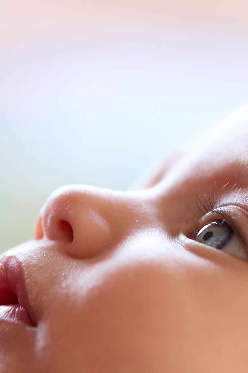 Extreme close-up portrait of a newborn baby with blue eyes and soft pastel background.