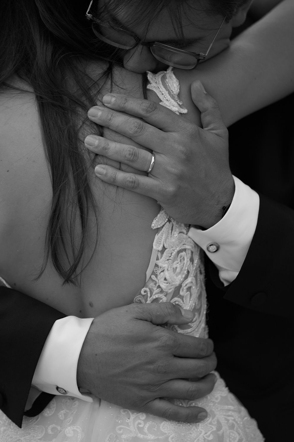 Close-up black and white wedding photo of groom embracing bride, showing wedding ring and cufflinks.