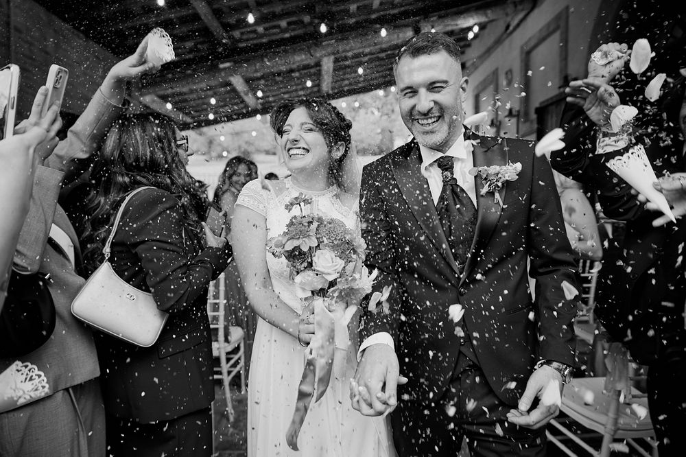 Black and white photo of joyful bride and groom walking through confetti shower at wedding reception.
