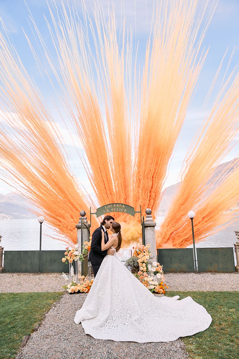 Bride and groom kissing under dramatic orange pampas grass arch at Locanda La Felice lakeside venue.
