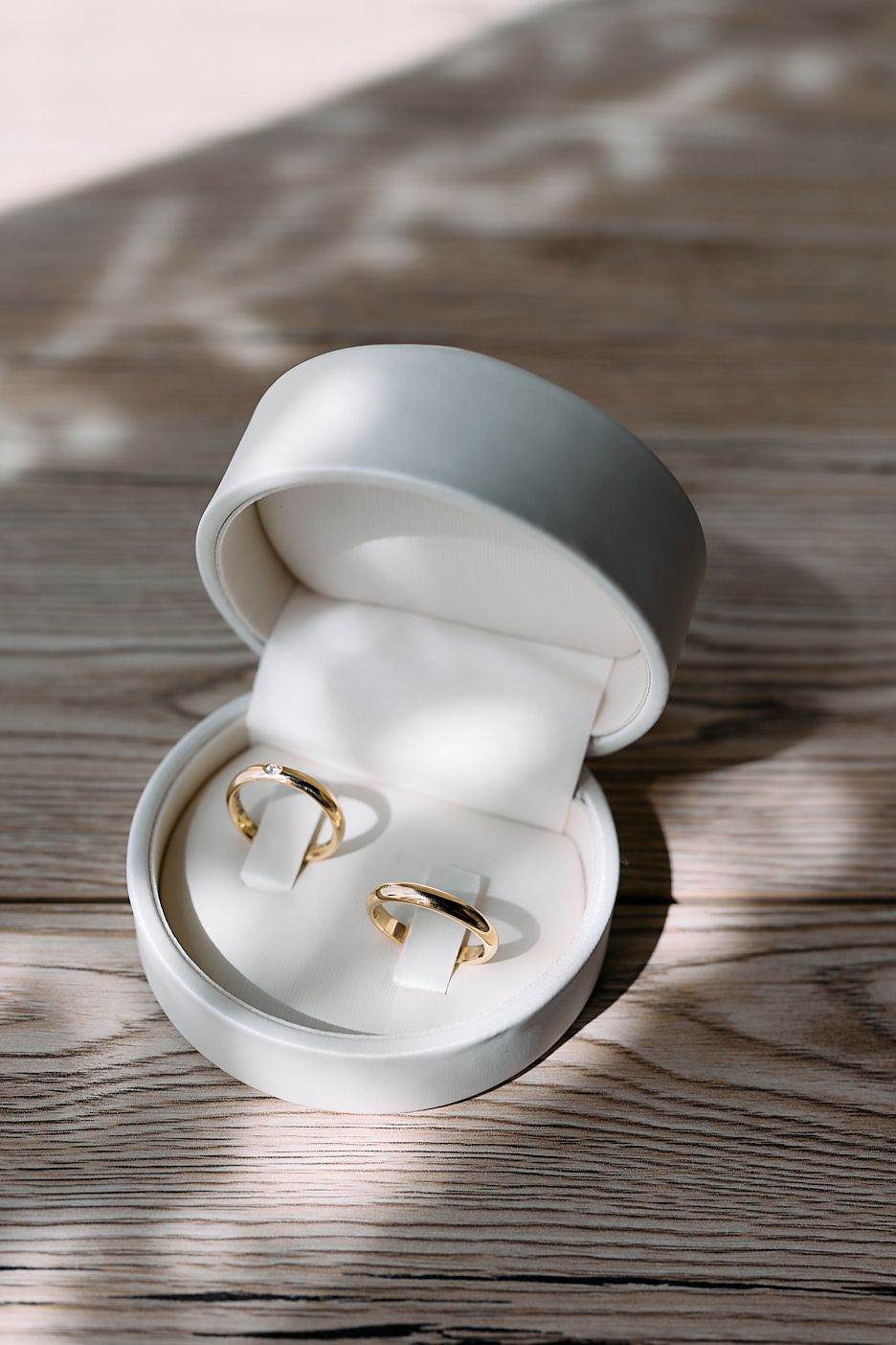 Two gold wedding bands displayed in an open white ring box on a wooden surface.