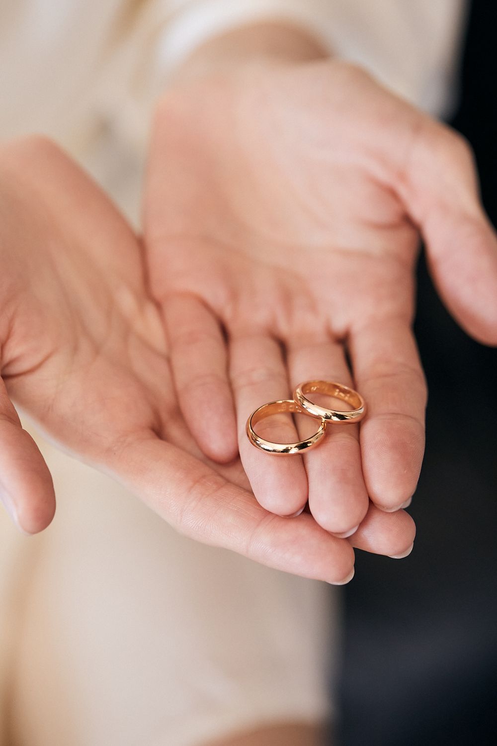 Close-up of two gold wedding bands resting in the open palms of a bride and groom.
