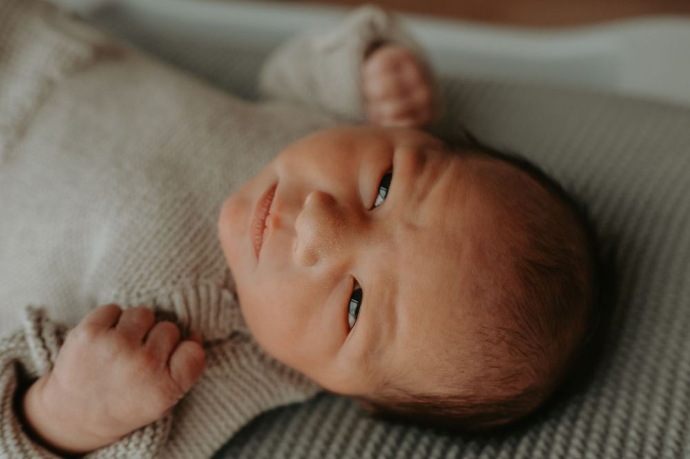 Close-up portrait of a peaceful newborn baby lying on a soft green knit blanket wearing a beige onesie.