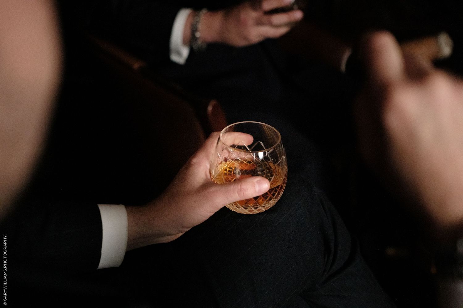 A man in a suit holding a glass of whiskey with ice at a formal event.