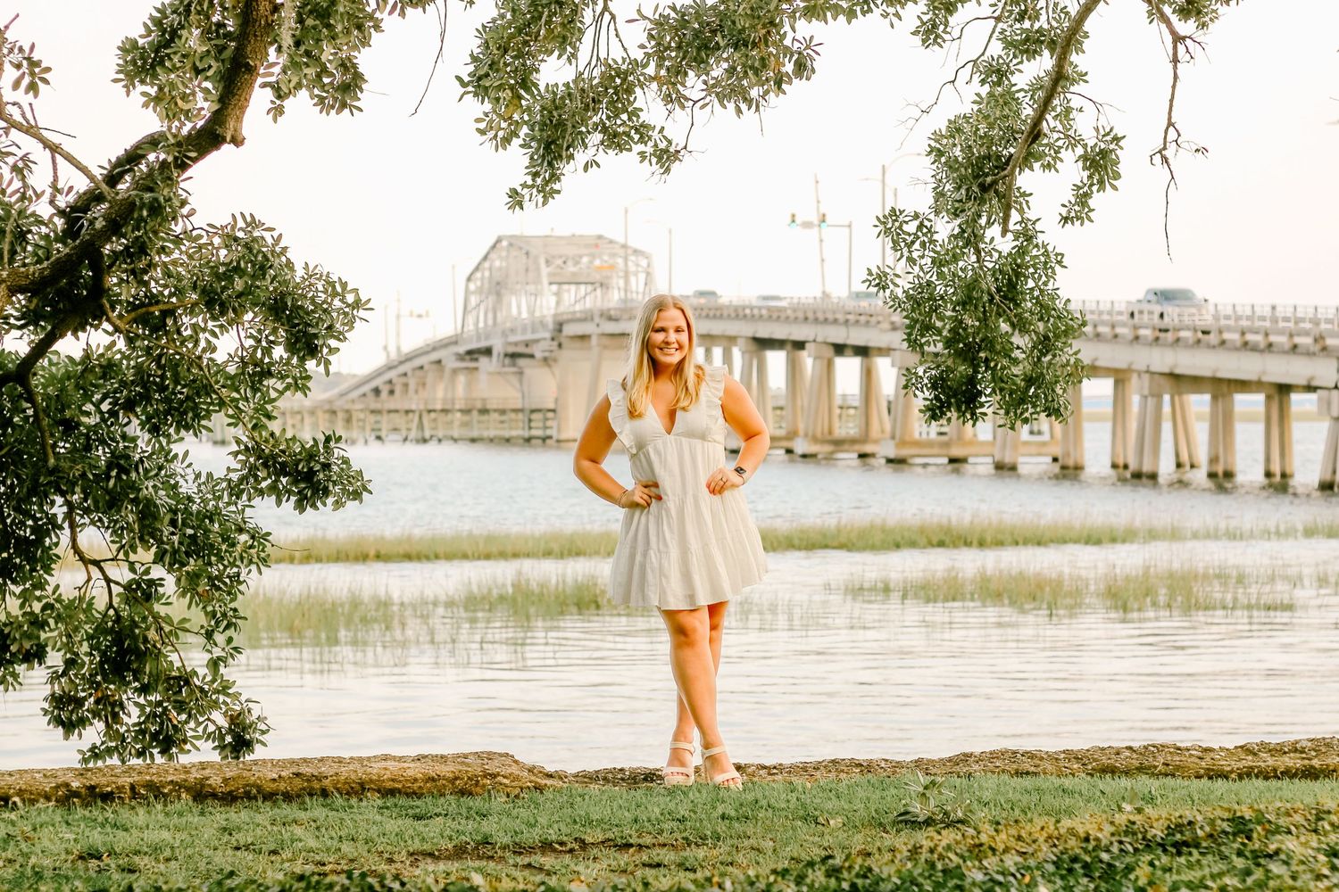 A sunset portrait by a waterfront with a bridge visible in the background.