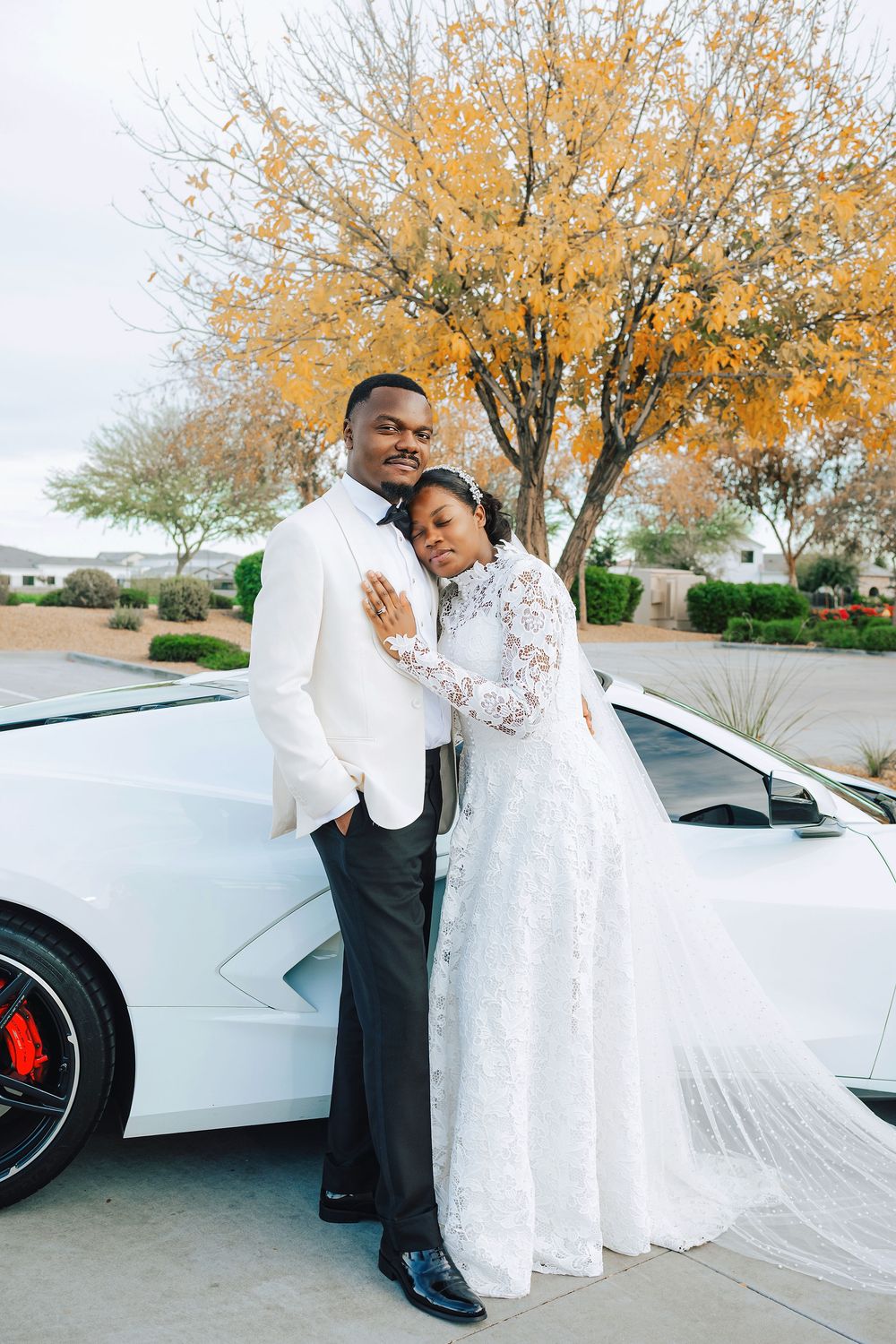 Elegant couple in wedding attire posing by a white Lamborghini with autumn foliage backdrop.