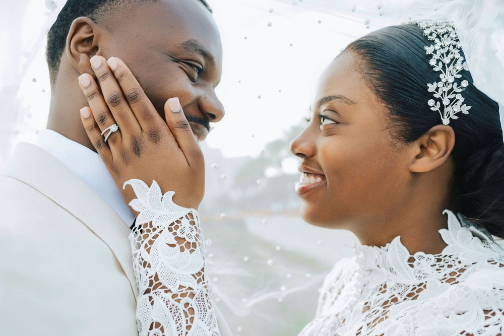 Black bride and groom share intimate moment, bride wearing lace dress and crystal hair piece.