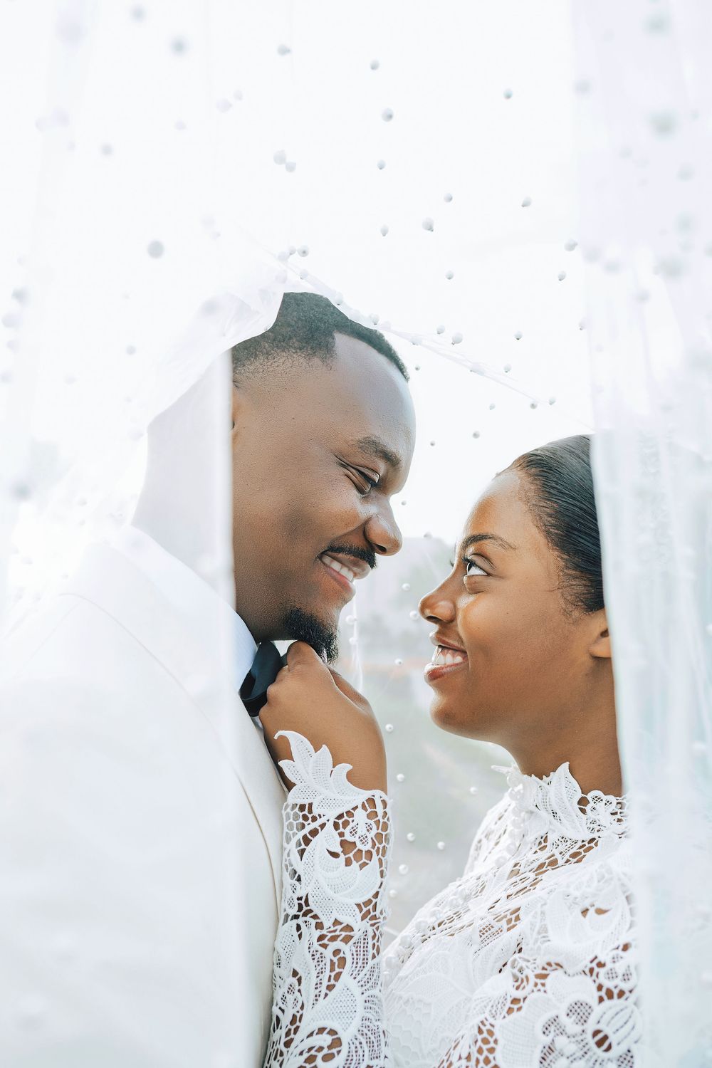 A joyful Black couple shares an intimate moment under a white lace veil on their wedding day.