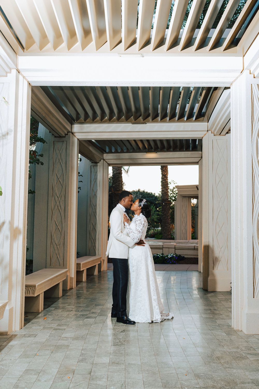 A bride and groom share a romantic kiss under an elegant pergola at their outdoor wedding venue.