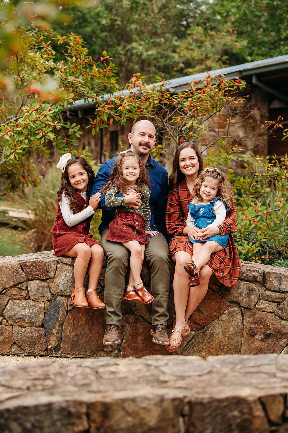 Happy family of five sitting on a stone wall surrounded by colorful autumn foliage.