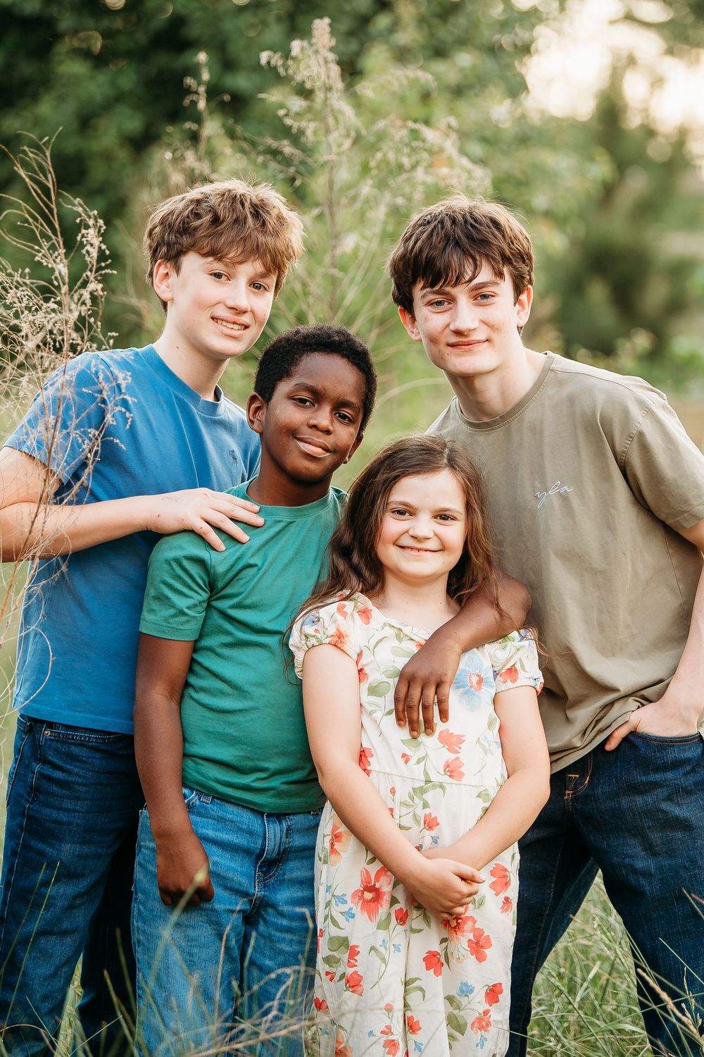 Four diverse kids smiling together outdoors in a lush green field at golden hour.