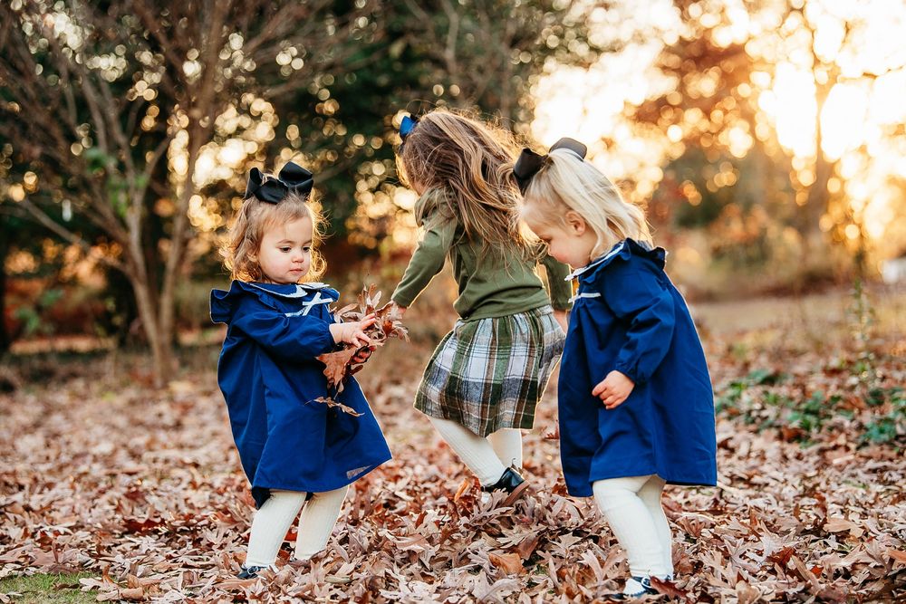 Three young sisters playing together in a pile of autumn leaves during a golden hour photo session.