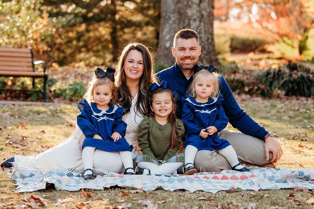 Smiling family of five sitting on a blanket among autumn leaves in a park for a fall portrait.