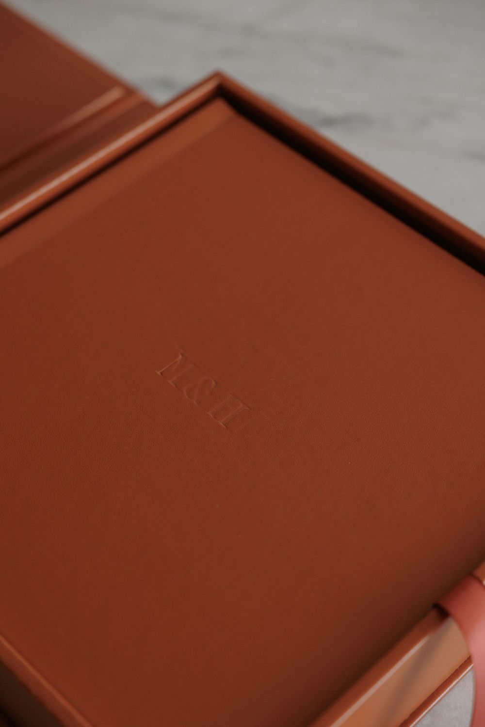 Brown leather monogrammed keepsake box with embossed initials, held by hand on marble surface.