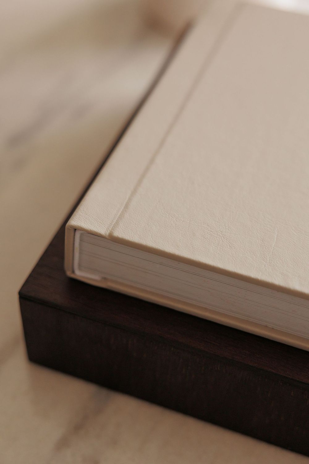 A cream linen hardcover book resting on a dark wooden box on a marble surface.