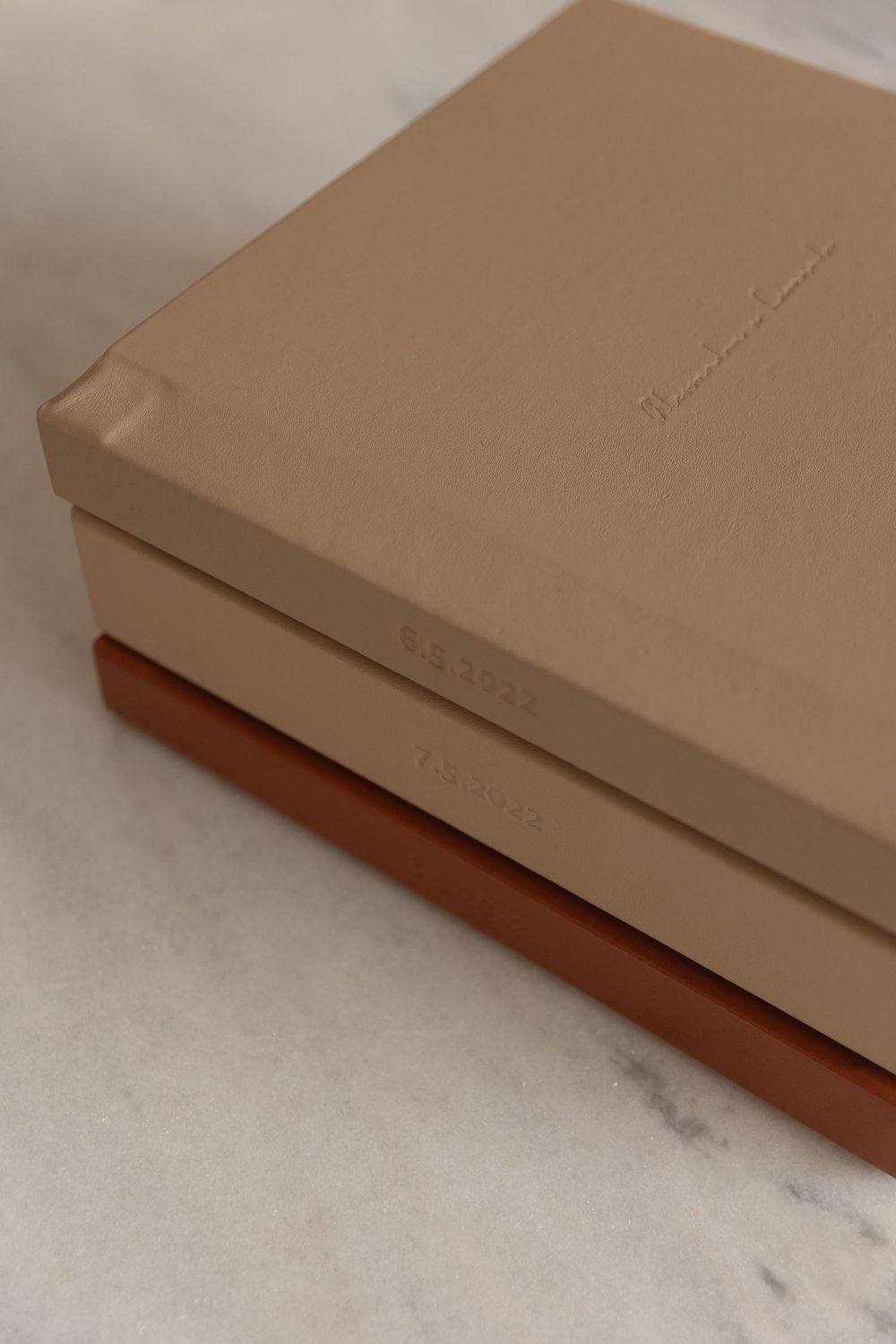 Three stacked neutral-toned boxes in beige and terracotta shades, displayed on a marble surface.