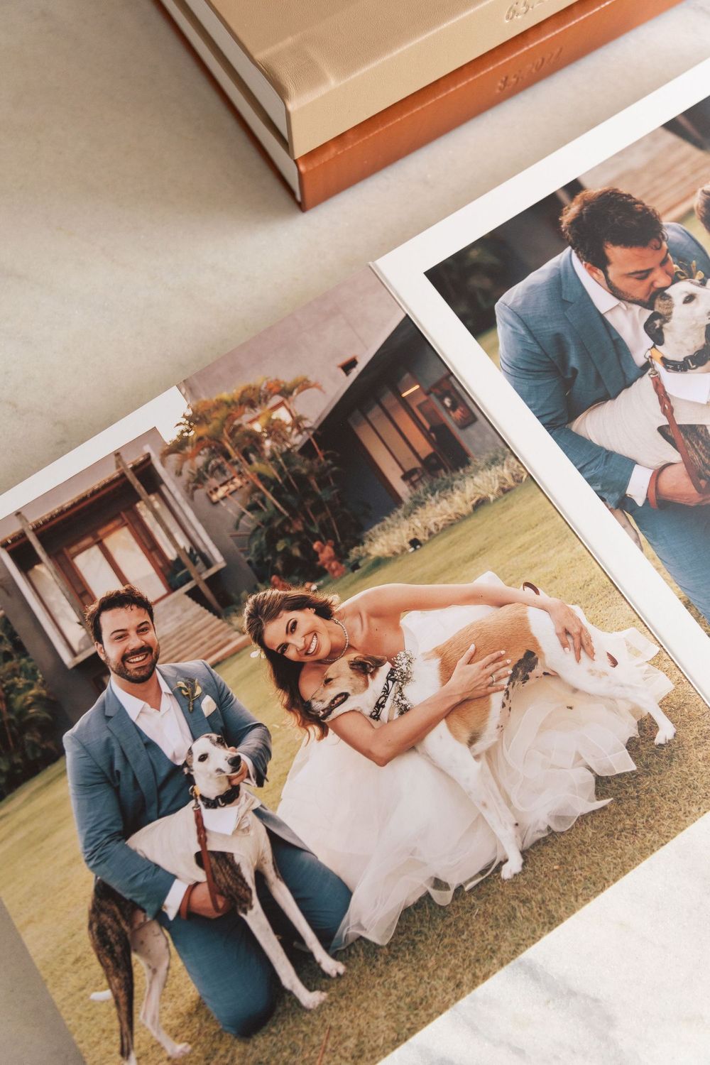 Open wedding photo album showing bride and groom posing with two dogs on green lawn, with a second photo of groom holding a dog.