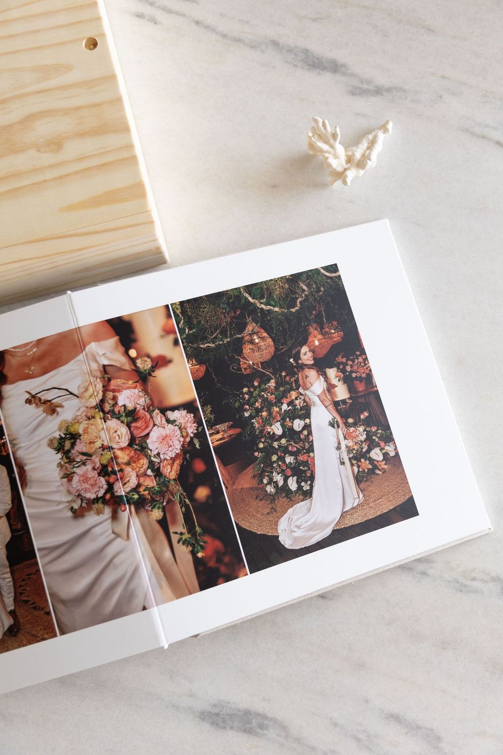 Wedding photo album open showing bride with floral bouquet and elegant venue decorations, displayed on marble surface.