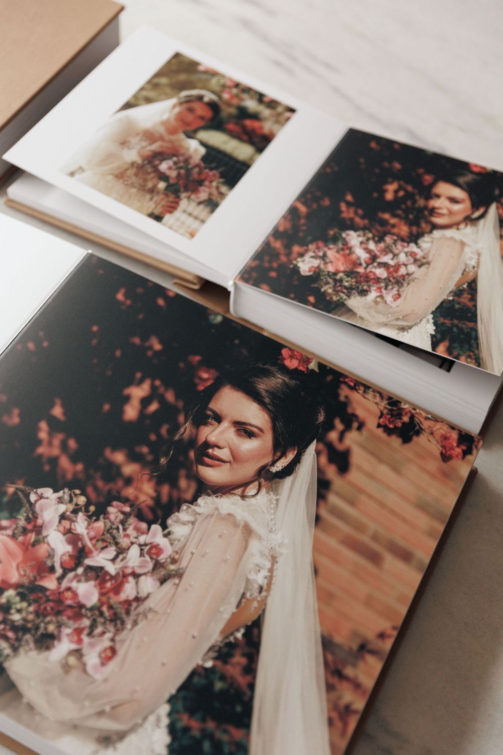 Elegant wedding photo albums open to reveal a bride holding a bouquet surrounded by pink blooms.