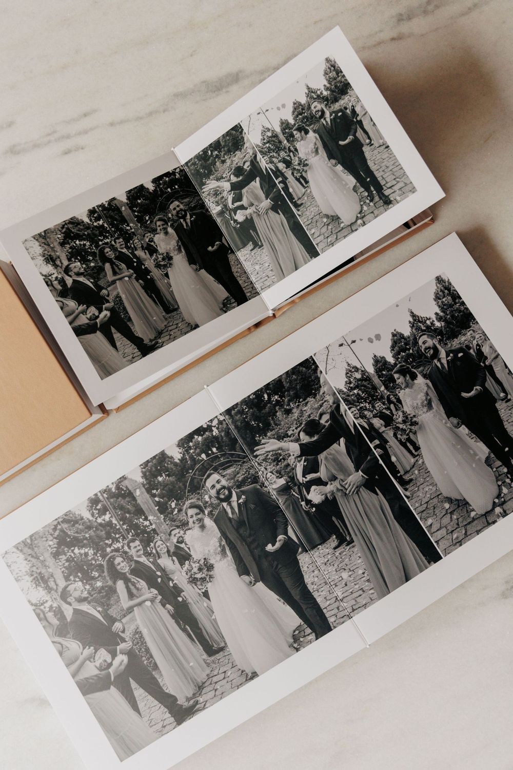 Two open wedding photo albums displaying black and white images of a bride and groom with guests outdoors.