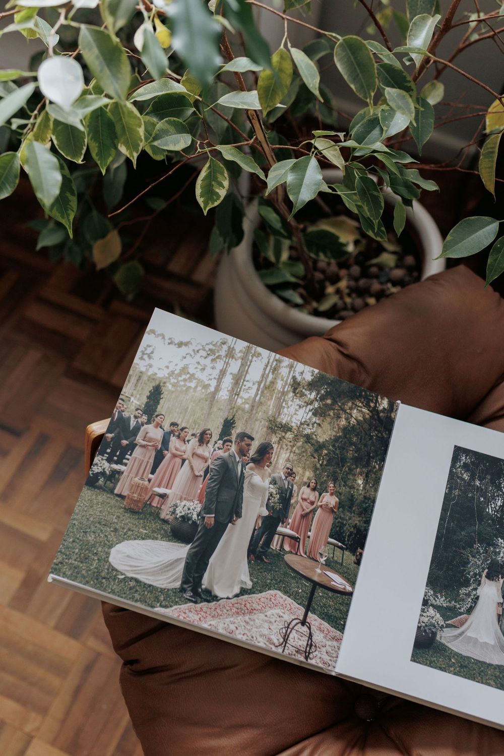 Open wedding photo album showing bride and groom ceremony with bridesmaids in pink dresses, displayed near a green potted plant.