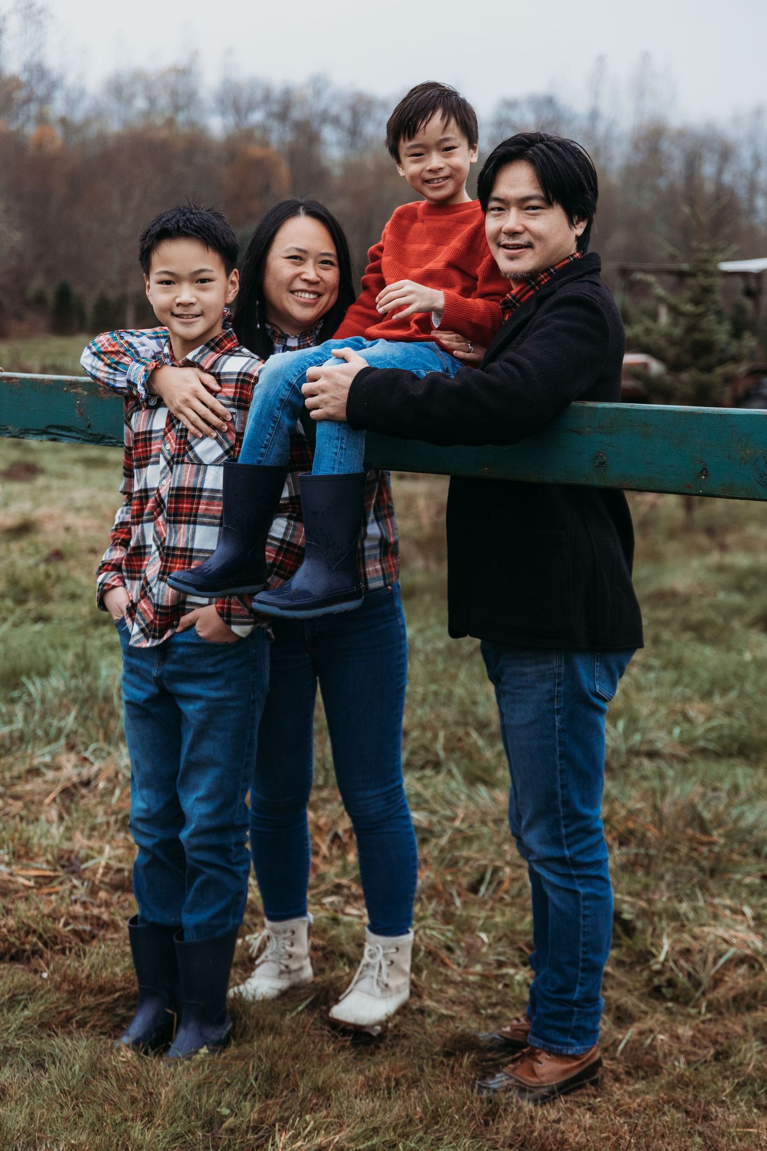 Family poses together outdoors in front of evergreen trees in warm autumn lighting.