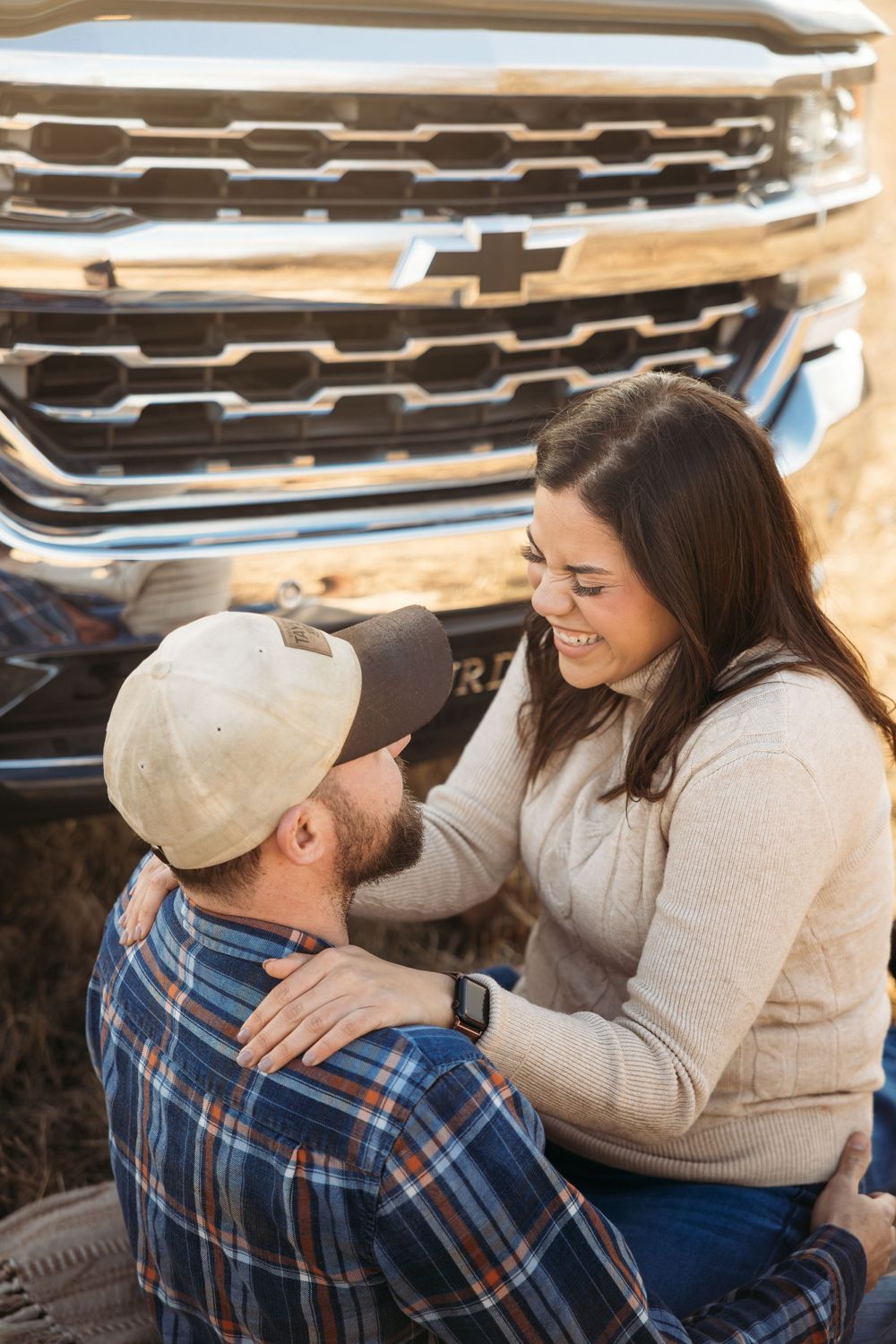 Couple sharing a joyful moment in front of a Chevrolet truck, woman smiling warmly at man in plaid shirt.